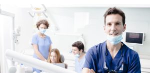 Dentists attending to patient, with one facing camera.